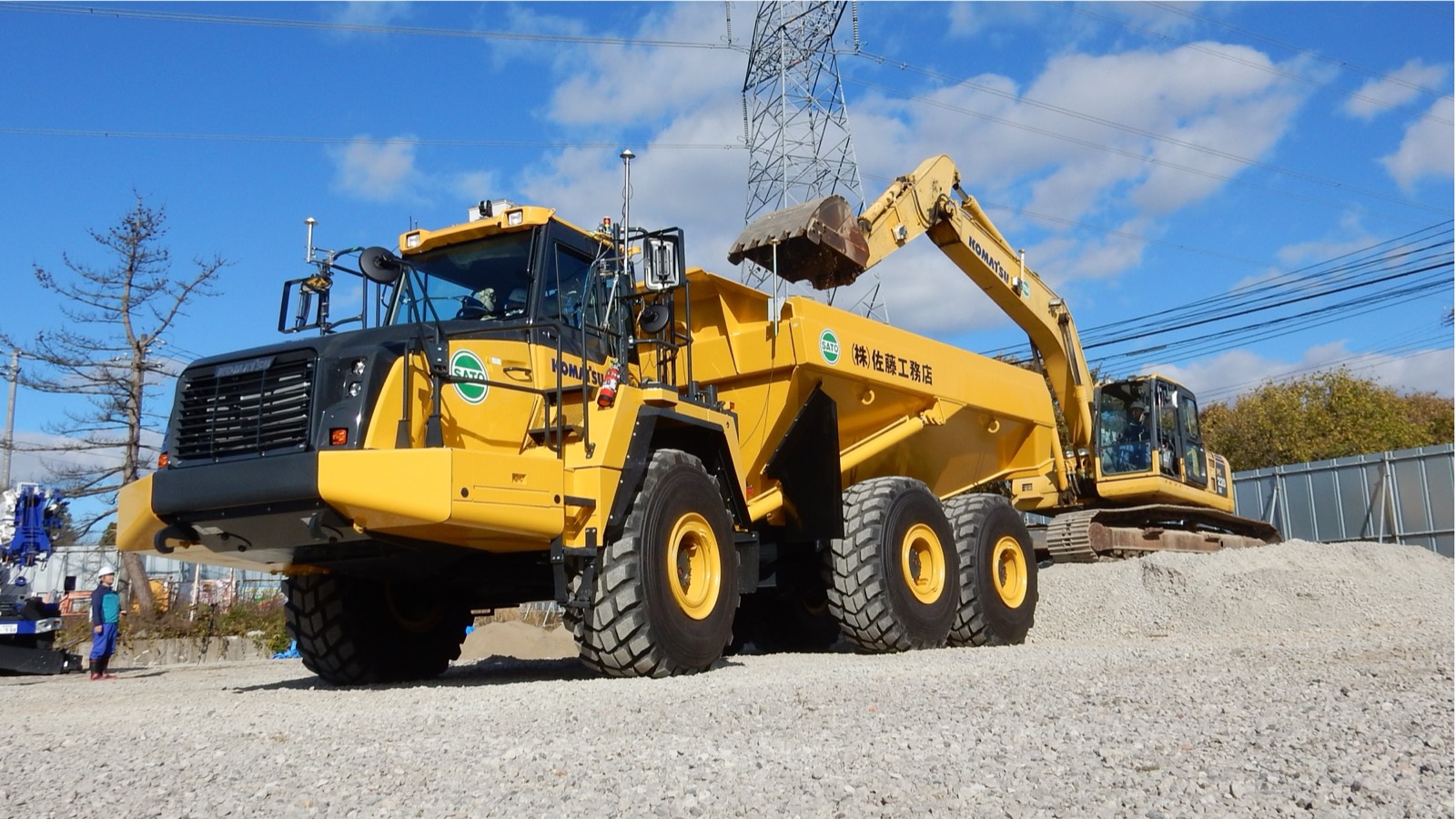 A yellow articulated dump truck being loaded by an excavator on a gravel construction site.